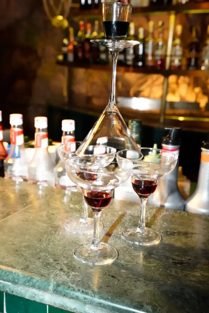 Mise en scène par le barman de plusieurs verres à cocktails ambiance rétro vintage moderne dans le bar extérieur du restaurant Rôtisserie de la paix à Marrakech Quartier Guéliz | Alba Photographe Restaurant Toulouse